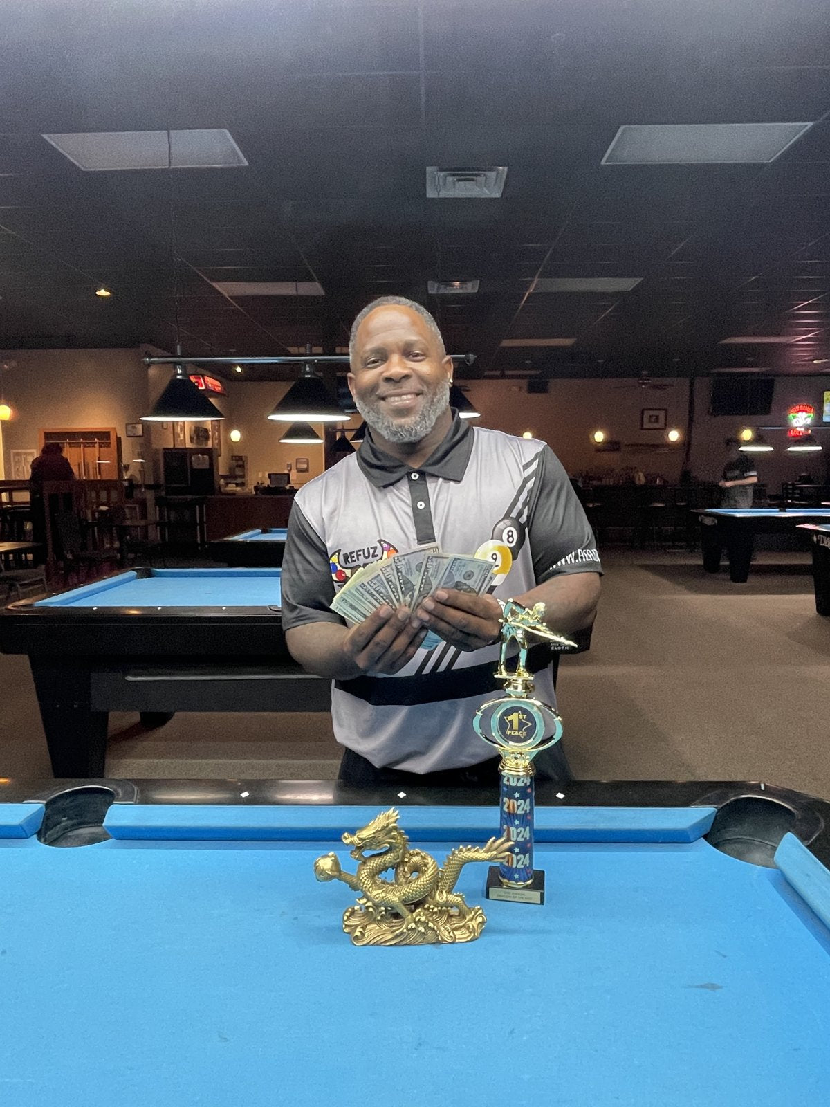 A Refuz Nation player holding his cash winnings and 2024 first-place trophy after a tournament win